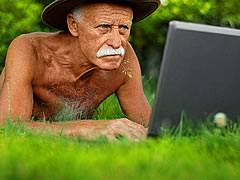 shirtless white-haired man in grass on computer